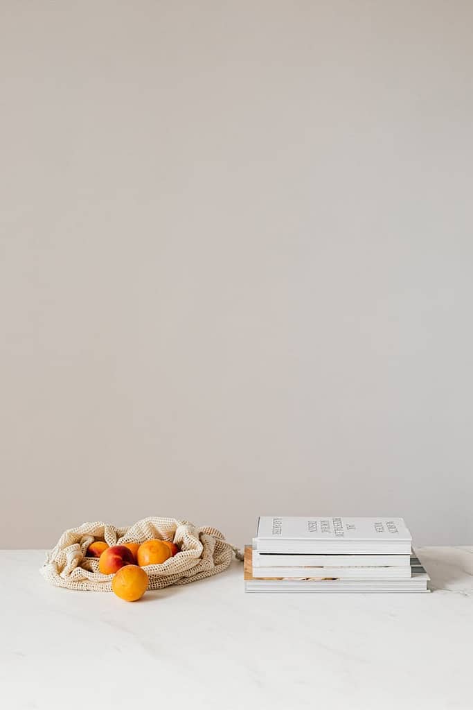 Composition of canvas bag with fresh ripe apricots placed on white table near stack of various books
